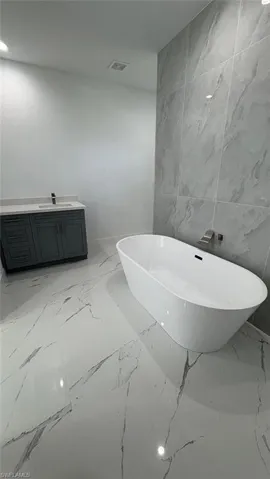 Full bath with marble finish floor, a soaking tub, visible vents, vanity, and stone wall