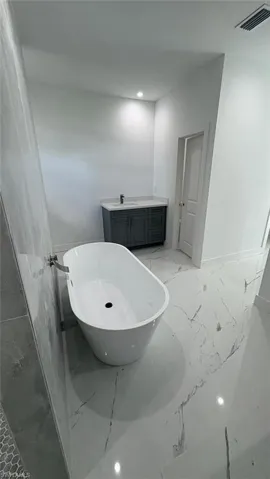 Full bathroom featuring marble finish floor, visible vents, a freestanding bath, and vanity