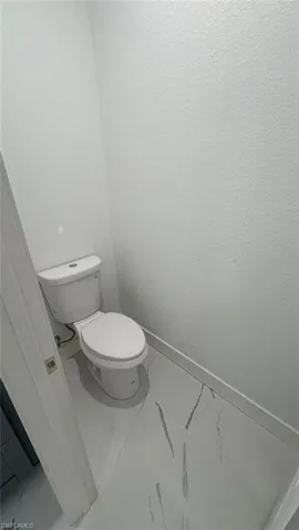 Bathroom featuring toilet, marble finish floor, and baseboards