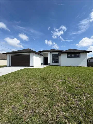 Prairie-style home with a garage, a front yard, driveway, and stucco siding
