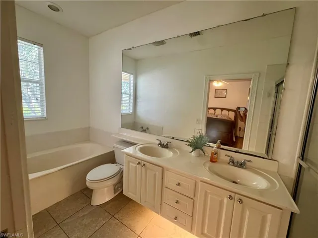 Full bath featuring double vanity, light tile patterned floors, and a bath