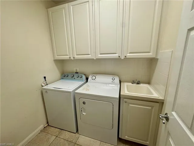 Laundry area with cabinet space, light tile patterned floors, and washer and clothes dryer