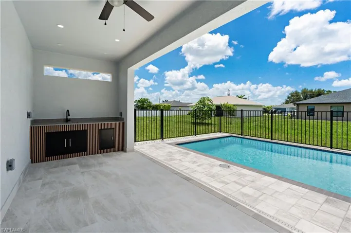Covered patio featuring an outdoor kitchen with a dark countertop, integrated sink, and wood-slat base cabinetry
