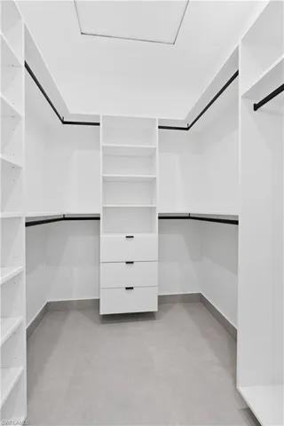 Walk-in closet featuring built-in shelving, hanging rods, an integrated drawer unit, and light gray tile flooring
