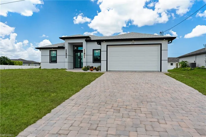 Contemporary stucco exterior featuring a paver driveway, an attached garage, a flat roofline, and a prominent glass entry door