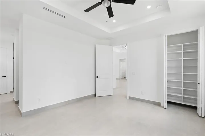 Spacious room with light-toned flooring, featuring a tray ceiling with recessed lighting and a ceiling fan