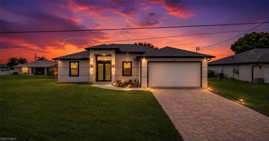 Contemporary stucco exterior featuring a paver driveway, an integrated garage, and a covered entry with double glass doors