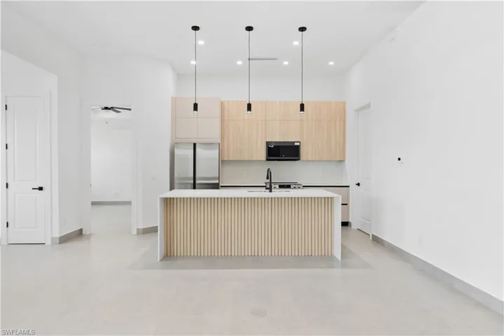Modern kitchen featuring a waterfall island with fluted paneling, light wood-finish cabinetry, stainless steel appliances, and sleek pendant lighting