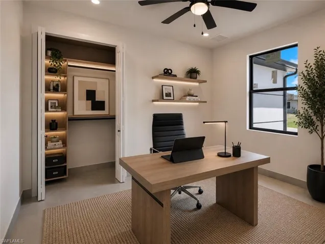 Dedicated office space featuring built-in closet shelving with integrated lighting, two wall-mounted floating shelves with accent lighting, a black-framed window, a ceiling fan with integrated lighting, and light-toned flooring