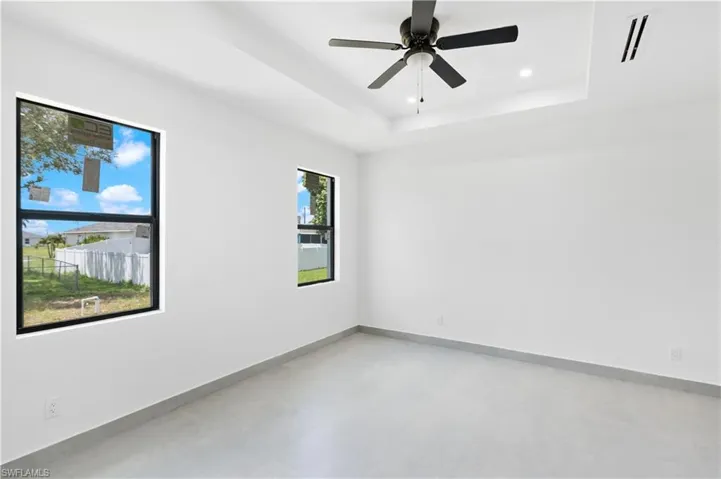 Spacious room featuring a tray ceiling with recessed lighting, a ceiling fan, two windows with black frames, and light-toned flooring