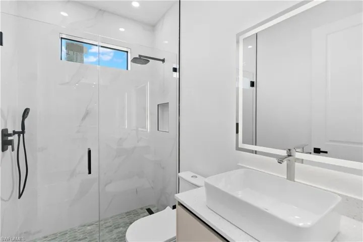 Contemporary bathroom featuring a spacious glass-enclosed shower with a rainfall showerhead and a separate handheld sprayer, complemented by white marble-patterned wall tiling and a pebble-tiled floor