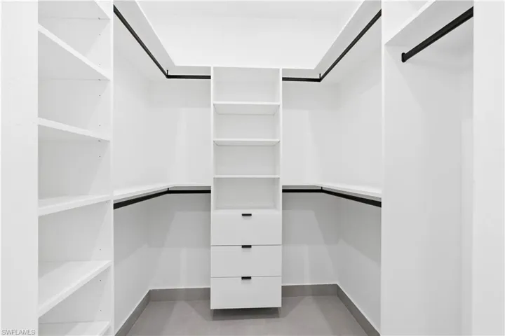 Walk-in closet featuring white built-in shelving, black hanging rods, and a central dresser unit with three drawers