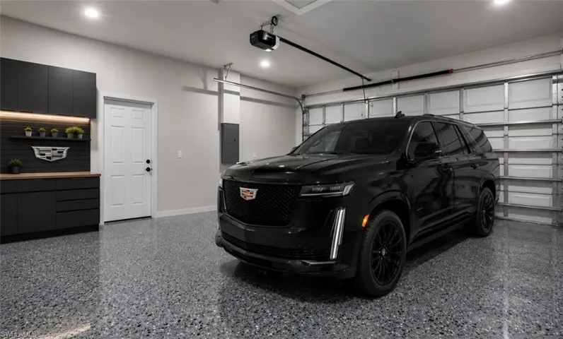 Garage featuring a speckled epoxy floor, built-in black cabinetry with wood-finish countertops, recessed lighting, and a white paneled entry door