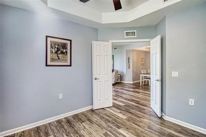 Empty room with dark wood-style flooring, a ceiling fan, visible vents, baseboards, and a tray ceiling
