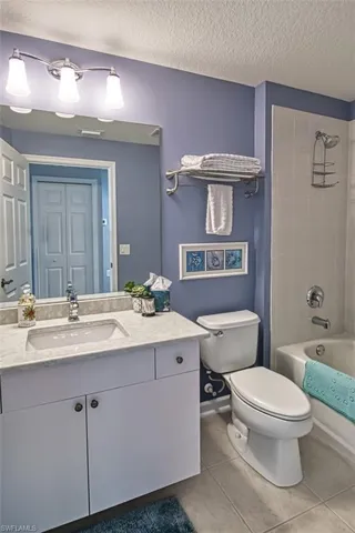 Bathroom with toilet, tile patterned flooring, a textured ceiling, vanity, and washtub / shower combination