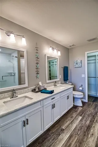 Full bath with double vanity, visible vents, a sink, and wood finished floors