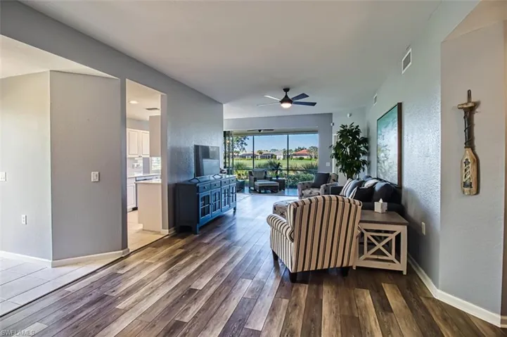 Living room featuring a textured wall, dark wood-type flooring, a ceiling fan, visible vents, and baseboards