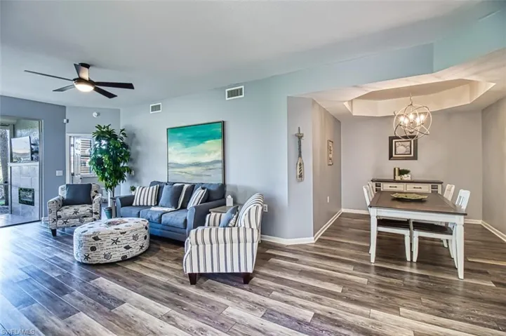 Living area featuring baseboards, visible vents, wood finished floors, and ceiling fan with notable chandelier