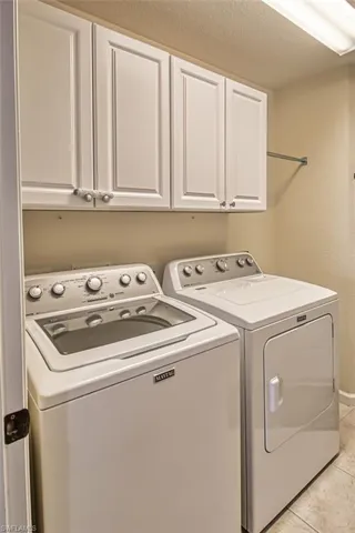 Laundry room featuring washing machine and dryer, cabinet space, a textured ceiling, and light tile patterned floors