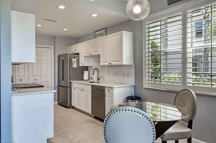 Kitchen featuring tasteful backsplash, stainless steel appliances, light countertops, white cabinetry, and a sink