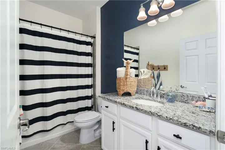 Bathroom with tile shower and floors, toilet, and large vanity