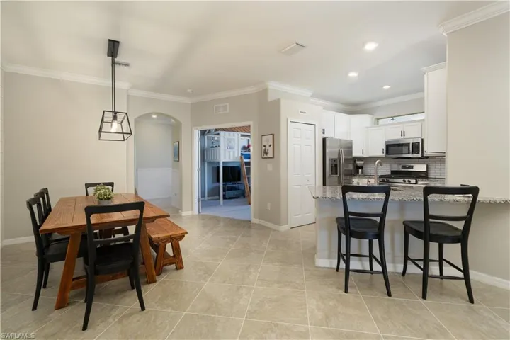 Kitchen featuring light stone countertops, appliances with stainless steel finishes, white cabinets, backsplash, and light tile flooring