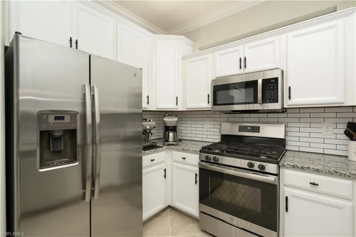 Kitchen with tile backsplash, appliances with stainless steel finishes, white cabinetry, and light tile flooring