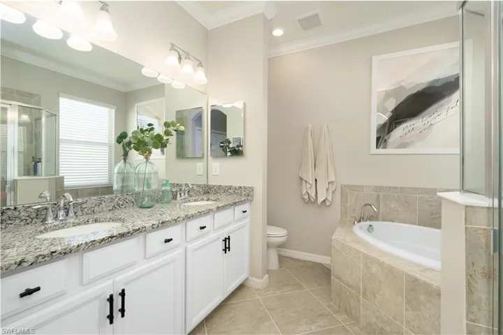 Bathroom featuring double vanity, tile flooring, ornamental molding, a relaxing tiled bath, and toilet