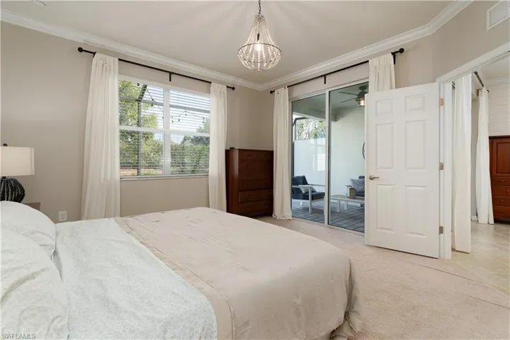Carpeted bedroom with an inviting chandelier, crown molding, and access to outdoor screened lanai space