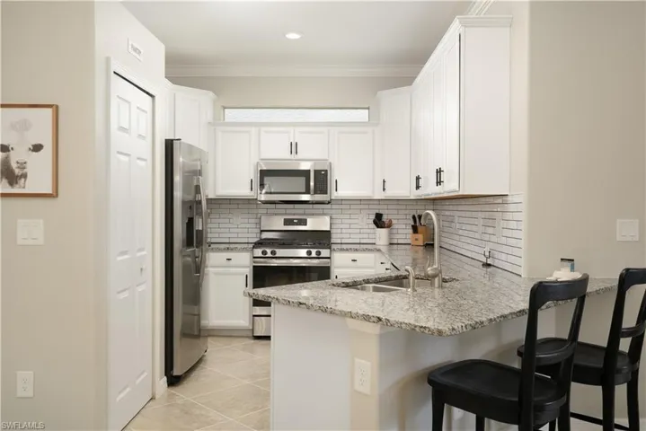 Kitchen featuring stainless steel appliances, light stone countertops, white cabinetry, sink, and light tile floors