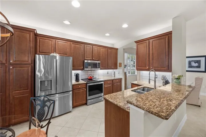 Kitchen with sink, appliances with stainless steel finishes, backsplash, light stone countertops, and kitchen peninsula