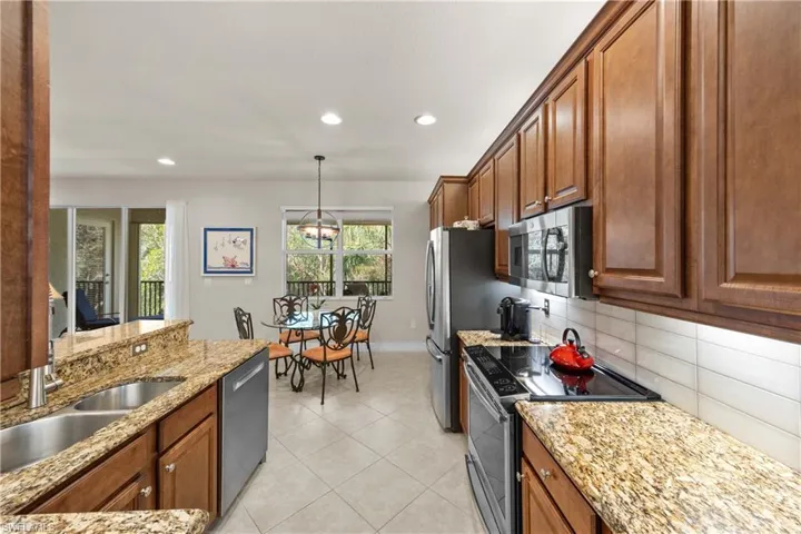 Kitchen featuring hanging light fixtures, light tile patterned floors, appliances with stainless steel finishes, light stone countertops, and decorative backsplash