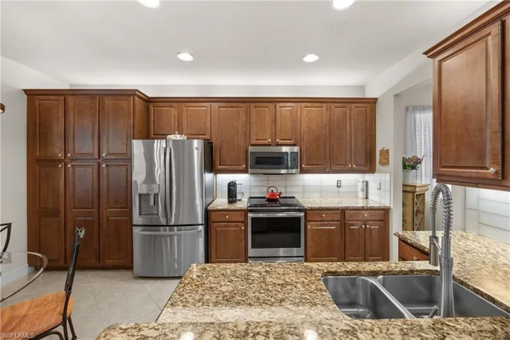 Kitchen with sink, backsplash, stainless steel appliances, and light tile patterned flooring