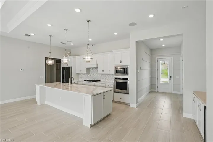 Kitchen with appliances with stainless steel finishes, decorative backsplash, white cabinetry, a kitchen island with sink, and recessed lighting