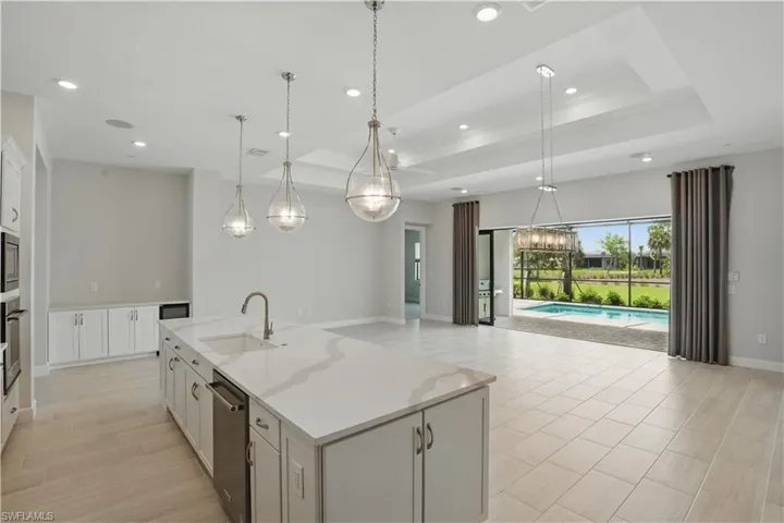 Kitchen featuring stainless steel appliances, a center island with sink, open floor plan, recessed lighting, and a raised ceiling