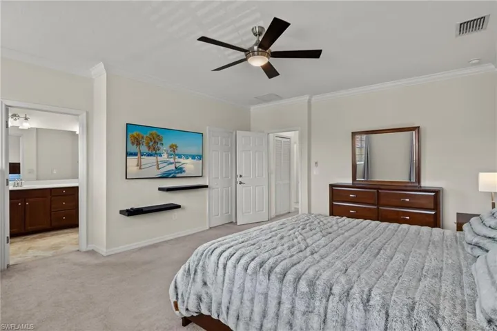 Bedroom with ceiling fan, crown molding, light colored carpet, and ensuite bathroom