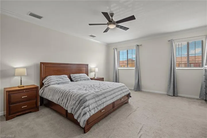Carpeted bedroom with ceiling fan and crown molding