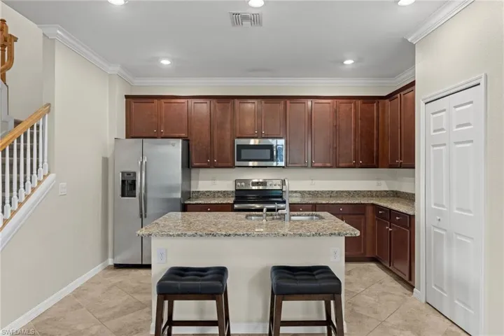 Kitchen with stainless steel appliances, sink, an island with sink, light stone countertops, and light tile patterned flooring