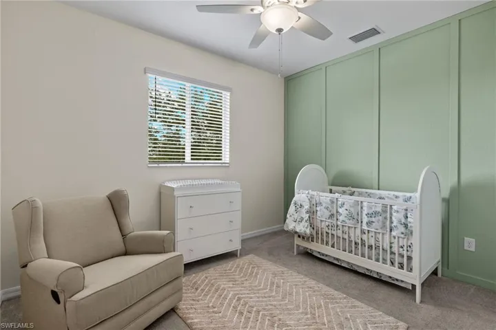 Carpeted bedroom featuring ceiling fan and a nursery area