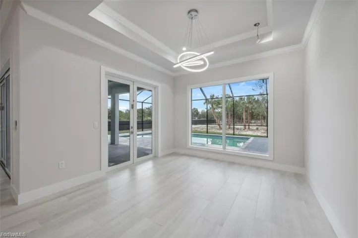 Empty room with hanging lights, light wood-type flooring, a tray ceiling, and crown molding