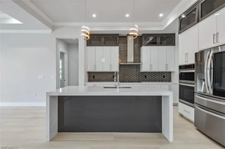 Kitchen with glass fronted cabinets, white cabinets, stainless steel appliances, hanging light fixtures, and light stone countertops