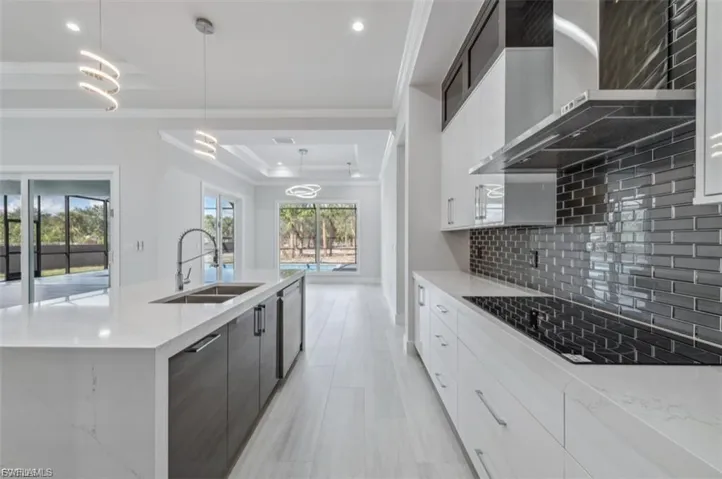 Kitchen featuring dual tone cabinets, a raised ceiling, hanging light fixtures, ornamental molding, and a large island with sink