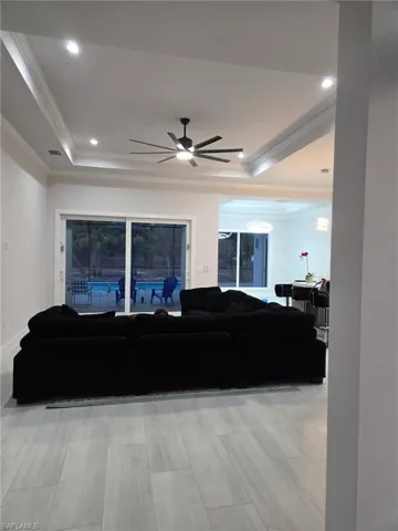 Living area with a raised ceiling, ornamental molding, ceiling fan, recessed lighting, and light wood-type flooring