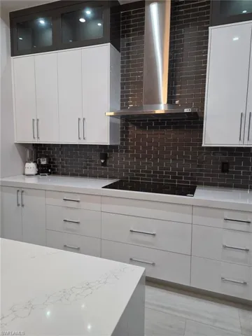 Kitchen featuring white cabinetry, light stone counters, backsplash, glass insert cabinets, and black electric stovetop