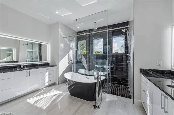 Full bathroom with a marble finish shower, a freestanding bath, and two vanities