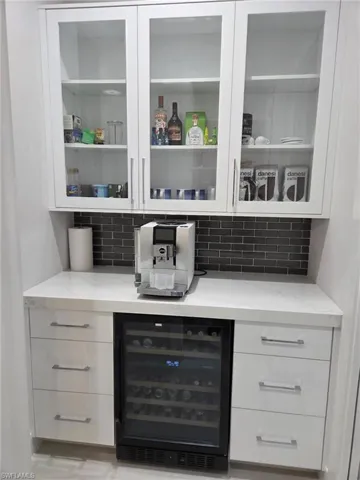 Bar with white cabinetry, decorative backsplash, beverage cooler, and light stone counters