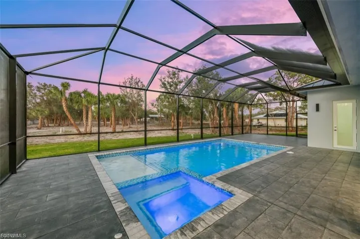 Relaxing pool / spa with a sunroom, a patio, a lawn, and a lanai
