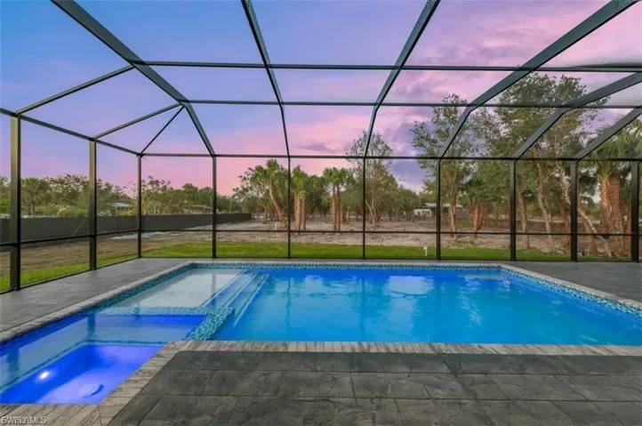 Pool at dusk with a sunroom, a yard, a lanai, and a pool with connected hot tub