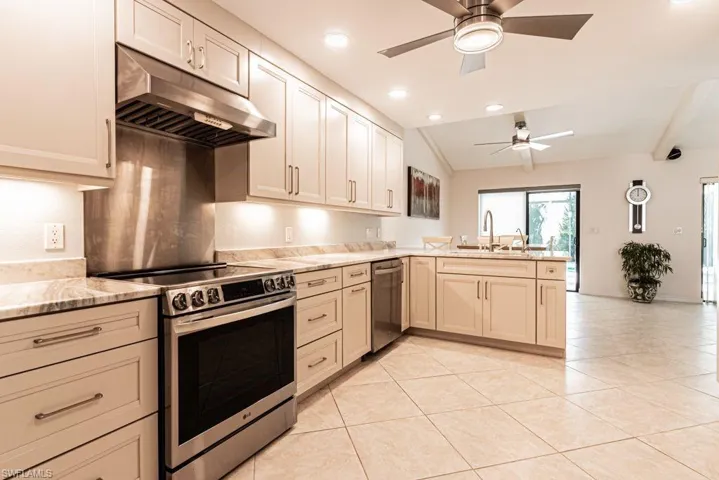 Kitchen featuring a peninsula, a ceiling fan, vaulted ceiling, under cabinet range hood, and stainless steel appliances