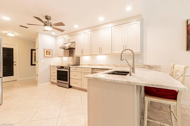 Kitchen with electric range, a peninsula, under cabinet range hood, light stone counters, and a sink